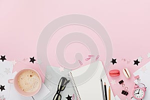 Fresh coffee, macaron, office supply, alarm clock and notebook on pink pastel table top view. Flat lay style. Cozy breakfast.