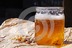 Fresh cold beer in a half liter glass jar and nuts on crumpled paper.