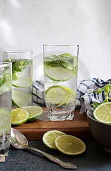Fresh cold cocktail Mojito with lime and mint in three glasses with water drops on a wooden stand with a towel and a spoon.