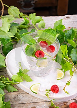 Fresh cold drink water, ice cubes, peppermint, lime, raspberry on a rustic table. Outdoor summer garden party, still life