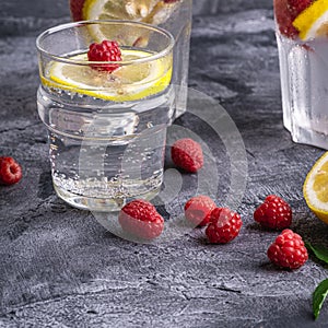 Fresh cold ice water drink with lemon, raspberry fruits and mint leaf in glass on stone concrete background