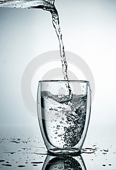 Fresh and cold, pure Water is poured into a glass. Purified water in a glass on a gray background. Motion freeze splash of crystal