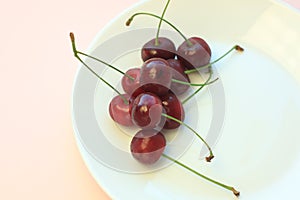 Fresh cold red cherries on white plate on powder pink background close-up. Copy space, minimalistic style