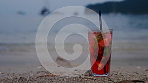 Fresh cold red color cocktail on tropical sandy beach with mountain view