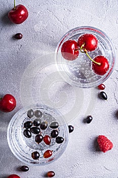 Fresh cold sparkling water drink with berries in two transparent glass on stone concrete background, summer diet beverage