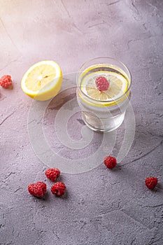 Fresh cold sparkling water drink with lemon, raspberry fruits in glass on stone concrete background, summer diet beverage