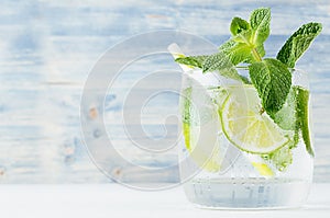 Fresh cold summer beverage with lime, leaf mint, straw, ice cubes on light blue wooden background, closeup.