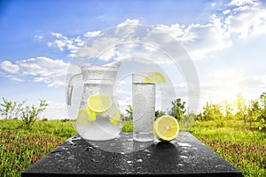 Fresh cold water with lemon and ice in a pitcher on the table.Homemade lemonade with fresh citruses on the background of nature.