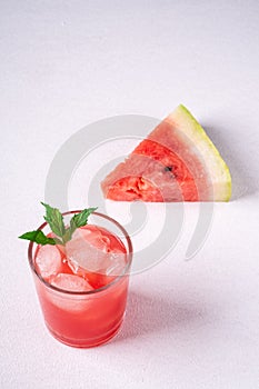 Fresh cold watermelon juice with ice cubes and green mint leaf in glass drink close to single slice of watermelon