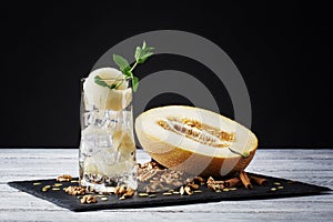 A fresh cold yellow mojito on a black background. A sweet beverage with pieces of melon, crushed ice and peppermint