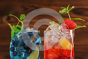 Fresh colorful cocktails with mint, lime, ice and berries on the wooden background. Two refreshing summer beverages. Copy space.