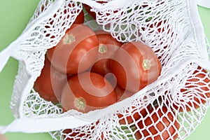 Fresh colorful heirloom veriety tomatoes in eco friendly mesh shopping bag on green background.