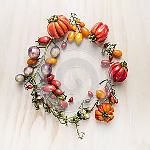 Fresh colorful tomatoes on branches with leaves, lined circle on a wooden background, top view