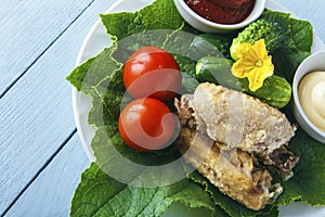 Fresh cooked delicious poultry wings on a green cucumber leaves with organic tomatoes on a white plate. View from above on wooden