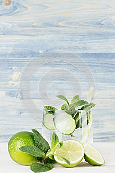 Fresh cool lemonade with mineral water, lime, cucumber, mint, ice and ingredients on light blue wood plank.