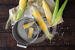 Fresh corn on the cob on wooden table with pan