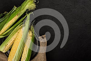 Fresh corn on cobs in plate over dark stone table. Food concept. Copy space top view