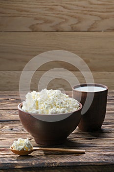 Fresh cottage cheese in  clay bowl with wooden spoon with a glass of milk on rustic wooden background