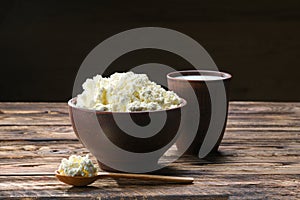 Fresh cottage cheese in  clay bowl with wooden spoon with a glass of milk on rustic wooden background