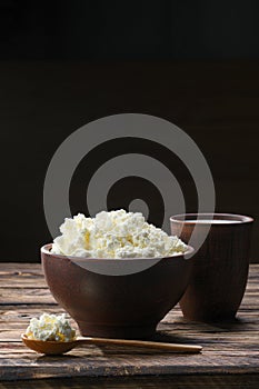 Fresh cottage cheese in  clay bowl with wooden spoon with a glass of milk on rustic wooden background