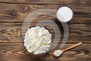 Fresh cottage cheese in  clay bowl with wooden spoon with a glass of milk on rustic wooden background