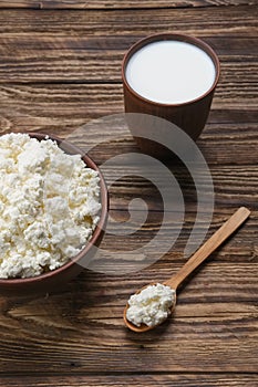 Fresh cottage cheese in  clay bowl with wooden spoon with a glass of milk on rustic wooden background