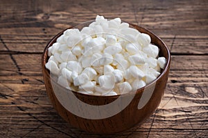 Fresh cottage cheese grain in a wooden bowl. Curd in granules with cream. Wooden rustic background. Copy space.