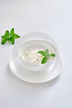 Fresh cottage cheese in granules in a white cup on a white background