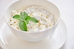 Fresh cottage cheese in granules in a white cup on a white background