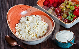 Fresh cottage cheese with juicy berries raspberries, strawberry and grapes on dark wooden background.