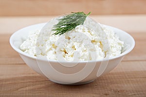 Fresh cottage cheese in a white bowl on a wooden board