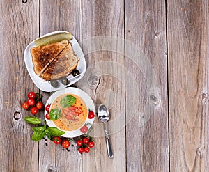 Fresh creamy tomato soup and sandwich with basil leaves on rustic wooden boards