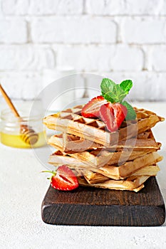 Fresh crisp Belgian waffles with ripe strawberries, mint and honey for breakfast