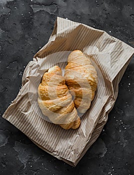 Fresh crispy croissants on a paper bag on a dark background, top view