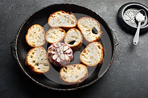 Fresh crispy crostini baguette slices with baked garlic, butter and cheese in a baking dish on a dark background. Top