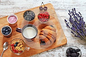 Fresh croissant, berries, yogurt, cornflakes and cup of milk on a wooden table.