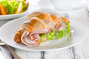 Fresh croissant with ham and salad leaf with sfresh salad on white wooden background
