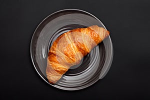 Fresh croissant in a plate on a black background. Top view, Homemade baked goods.