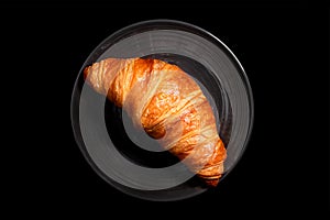 Fresh croissant in a plate, isolated on black, top view. Homemade baking