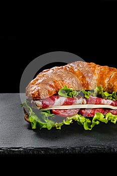 Fresh croissant sandwich with meat and vegetables on black background