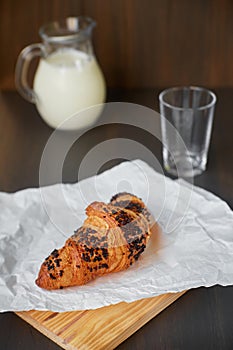 Fresh croissant on white crumpled paper and a wooden board with a decanter and a glass of milk. Freshly baked croissant on a dark