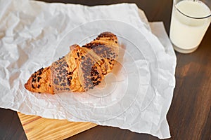 Fresh croissant on white crumpled paper and a wooden board with a glass of milk. Freshly baked croissant on a dark wooden table.