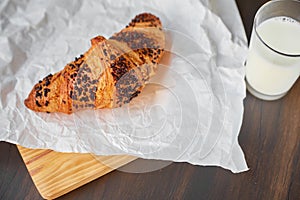 Fresh croissant on white crumpled paper and a wooden board with a glass of milk. Freshly baked croissant on a dark wooden table.