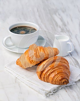 Fresh croissants bread and a cup of coffee on marble table.