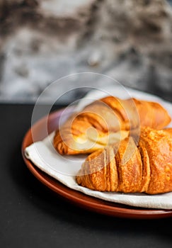 Fresh croissants on a clay plate on a dark background