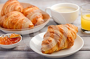 Fresh Croissants with coffee, jam and orange juice for breakfast on rustic wooden background.