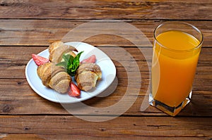 Fresh croissants and a glass of orange juice on a wooden table.