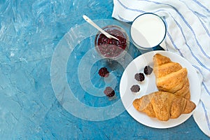 Fresh croissants with jam and a glass of milk on a light blue background. French breakfast. Top view. Copy space.