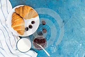 Fresh croissants with jam and a glass of milk on a light blue background. French breakfast. Top view. Copy space.