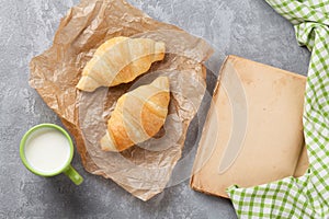 Fresh croissants, milk and old book